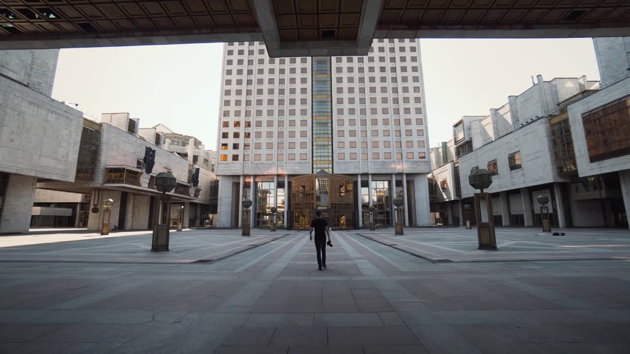 Hombre caminando en una plaza de la ciudad rodeado de edificios