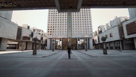 man walking in a city square surrounded by buildings.