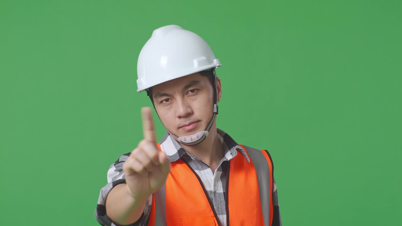 Close Up Of Asian Male Engineer With Safety Helmet Disapproving With No Index Finger Sign While Standing In The Green Screen Background Studio