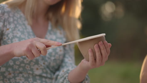 a young woman is intently sculpting an object from clay in an open area in nature enjoying the process of close-up. the girl taps the clay product with a spatula a tool.