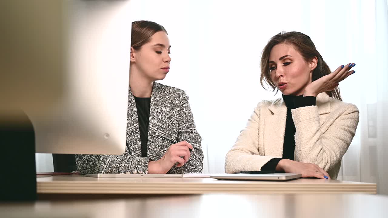 Attractive young adult women work together in the office at a meeting. A new employee consults with a mentor and presents a new project. Open space concept for teamwork