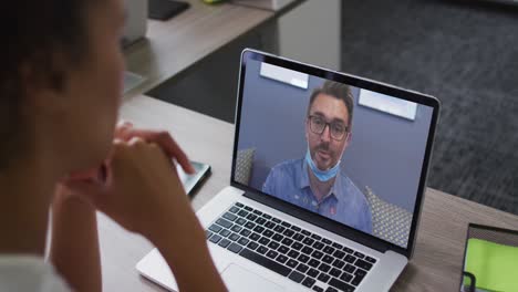 sección media de una mujer afroamericana haciendo una videollamada con un colega masculino en una computadora portátil en la oficina