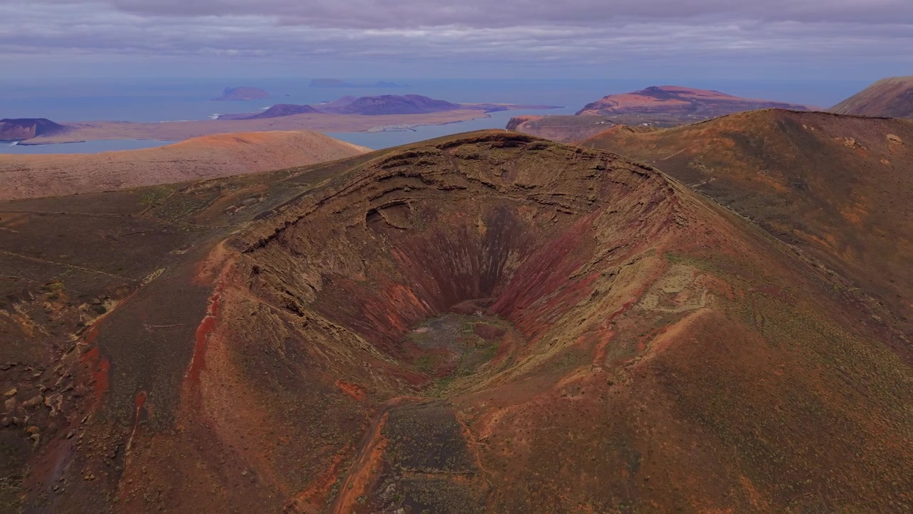 Cratere colorato di un vulcano dormiente a Lanzarote, con l'isola La Graciosa visibile all'orizzonte, Spagna. Ripresa aerea all'indietro