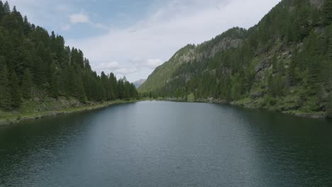 Ascending-drone-flight-over-mountain-lake-and-green-trees-with-waterfall---Tilt-down