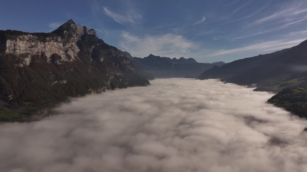 Aerial view above cloud layers with majestic Swiss Alps surrounding Walensee, Amden. Stunning misty mountain landscape.