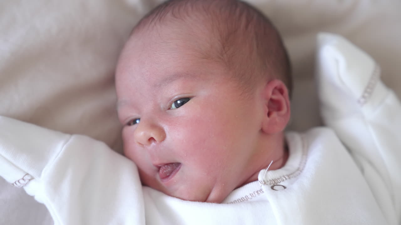 Lovely newborn baby portrait. Face of an infant baby laying on a bed. Hungry little child looking for mother. Cute little child.
