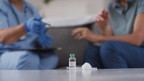 midsection of african american female doctor talking with female patient at home with vaccination in