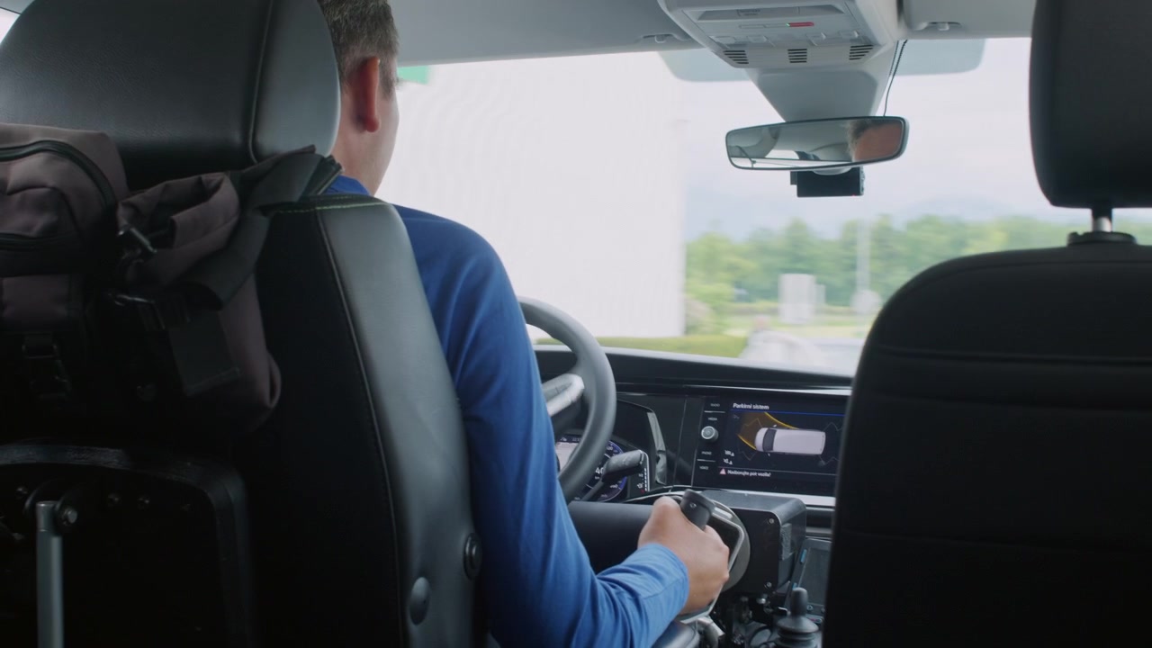 Vista trasera de un conductor con discapacidad operando controles manuales y tecnología de asistencia en un vehículo adaptado