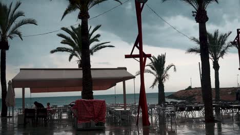 few people in an open pavilion by the sea in vinaros, spain on a stormy weather - wide shot