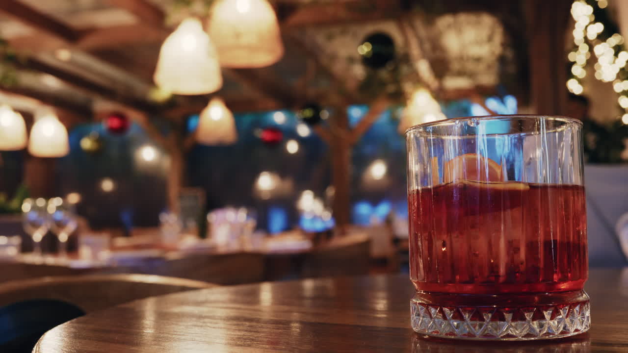 Bicchiere di cocktail rosso su un tavolo di legno all'interno di un ristorante con illuminazione calda