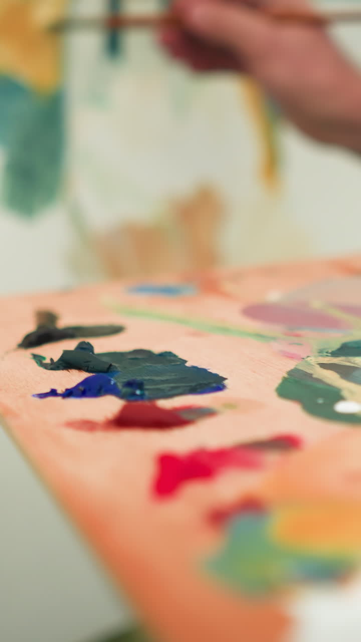 A painter holds a wooden palette full of vibrant paint colors while adding the final touches to a canvas. focusing on the palette filled with mixed paints and the delicate motion of the brush