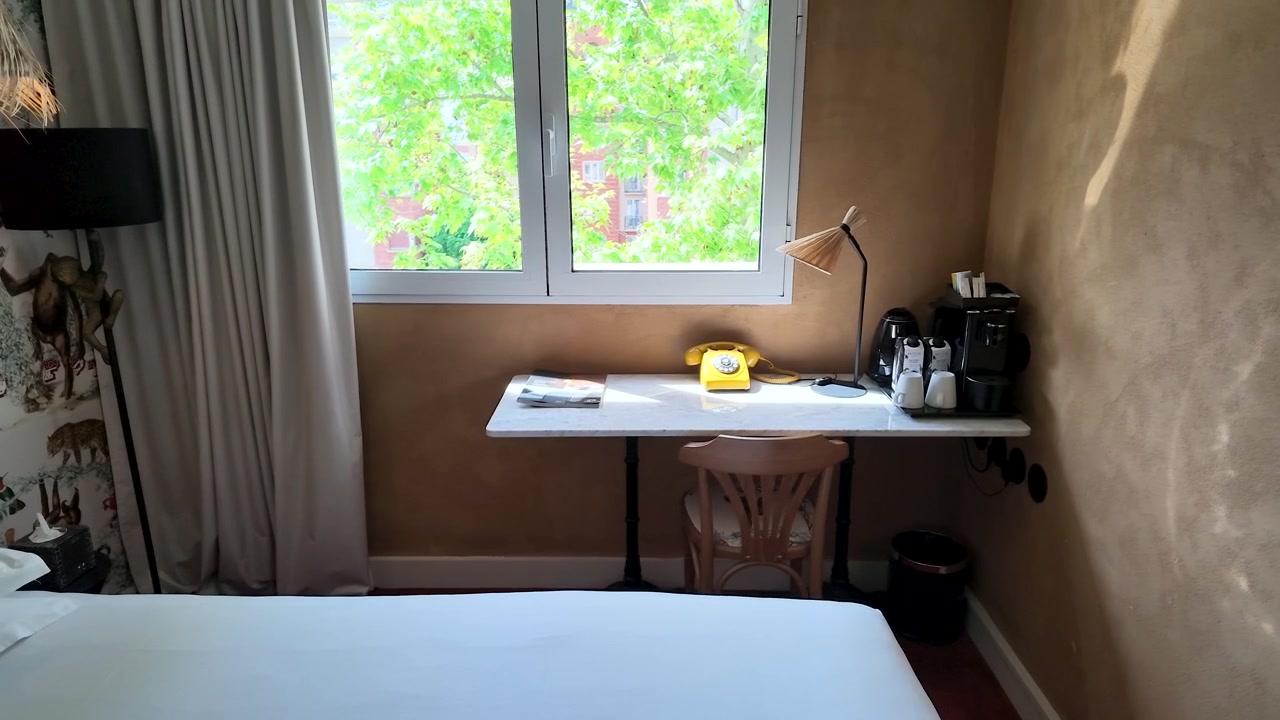Static wide shot of a stylish hotel room featuring a desk, rotary phone, and window