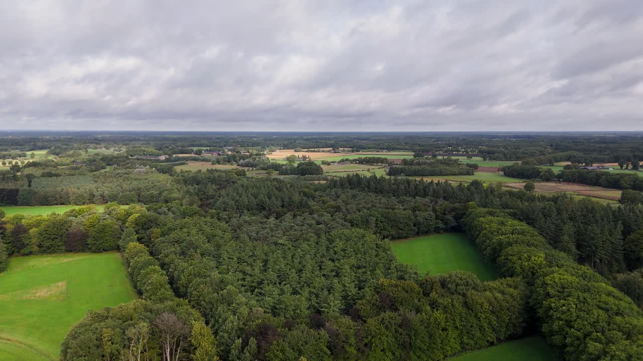 Aerial view of a landscape with forest, fields, and cloudy sky