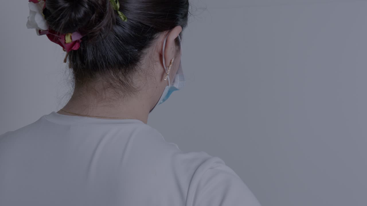 A woman wearing a mask examines an empty freezer in a dimly lit kitchen, capturing a sense of scarcity and resilience during uncertain times. Rear view, focus on the freezer