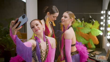 three cabaret girls in colorful dance gowns taking a selfie photo