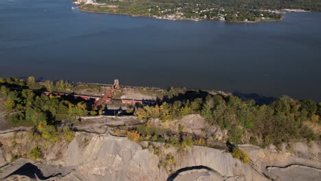 an aerial view over train tracks as a long cargo train goes by next to the hudson river in upstate ny