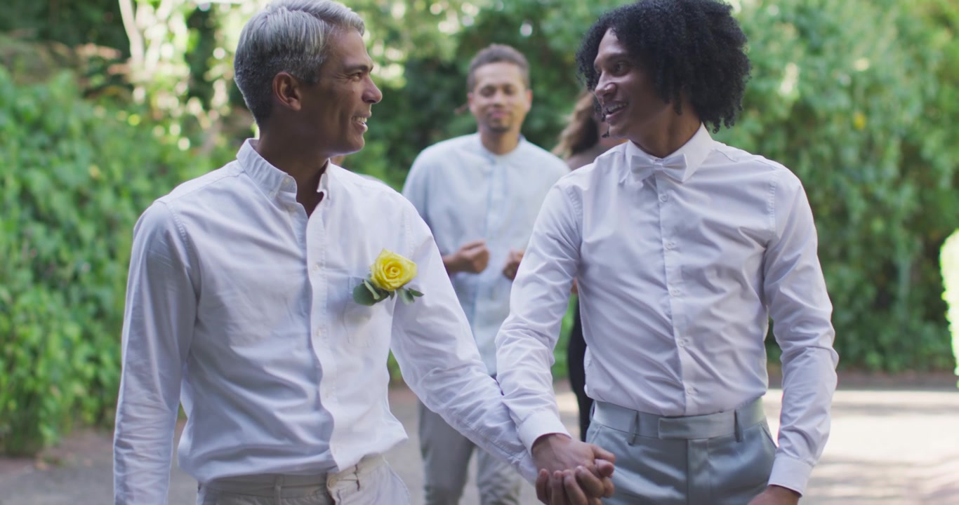 Video verticale: Due uomini afroamericani camminano mano nella mano su un sentiero in giardino, celebrando un matrimonio.