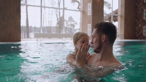 happy father and his little daughter is swimming together in pool of modern new wellness center