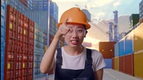 close up of asian woman worker wearing goggles and safety helmet shouting to camera while standing at container yard warehouse