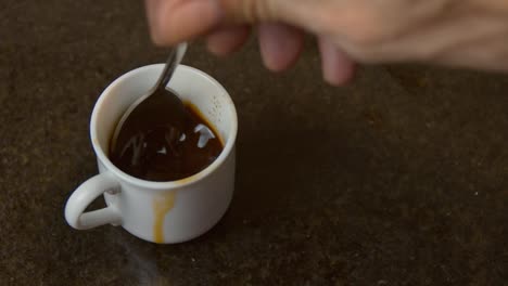 coffee in white mug being stirred with metal spoon, close up