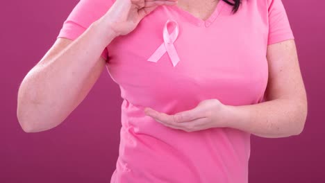 Video-of-midsection-of-caucasian-woman-wearing-pink-cancer-awareness-ribbon,-with-pink-background