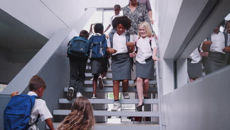 teacher and pupils walking down stairs in busy elementary school corridor