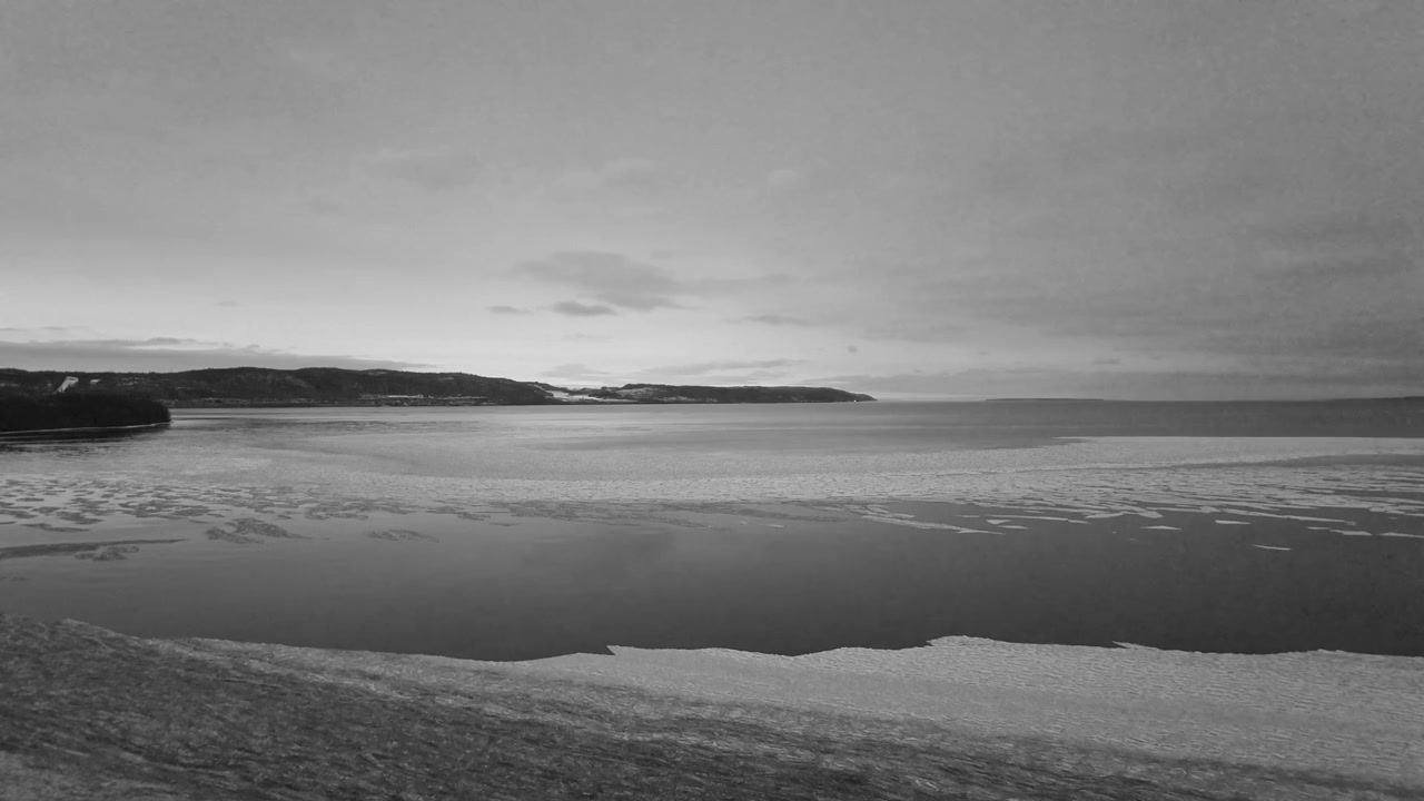 Drone aerial footage of Lake Vättern, Sweden, showcases dramatic black and white winter scenery with unique ice formations, tranquil water, and a cloudy sky. No people, cold moody light.