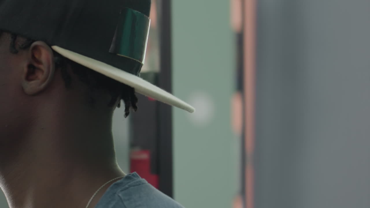 Close up side profile of college student in backward cap by library shelves, sorting book with focused expression, soft blur background and muted colors capturing quiet study mood