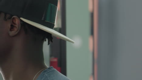 close up side profile of college student in backward cap by library shelves, sorting book with focused expression, soft blur background and muted colors capturing quiet study mood