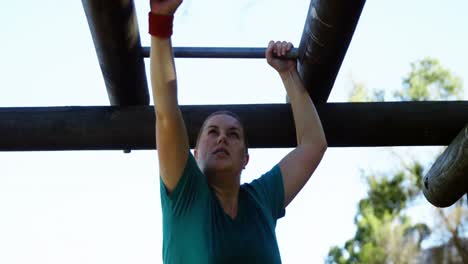 determined woman exercising on monkey bar during obstacle course