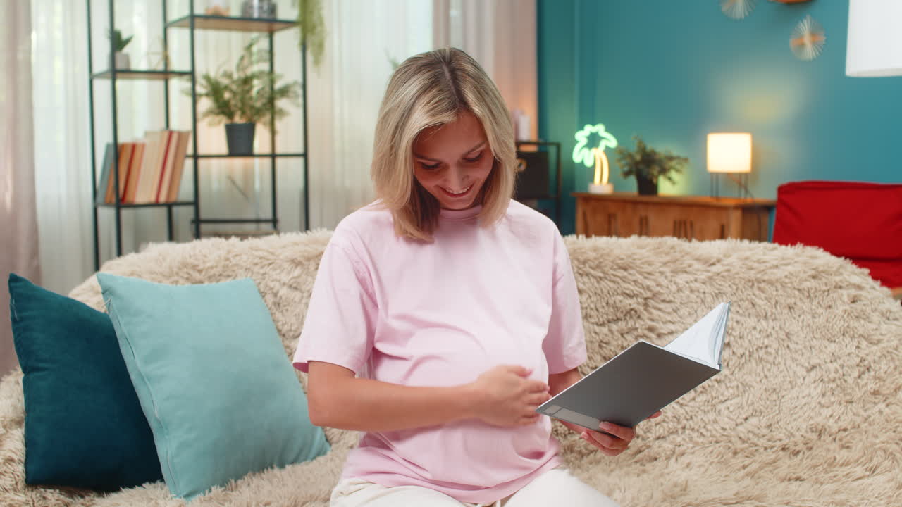 Pregnant woman raises finger in eureka moment writing baby name idea in diary smiling brightly happy