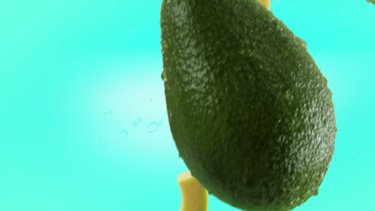 aguacate con rebanadas y salpicaduras cayendo sobre un fondo turquesa