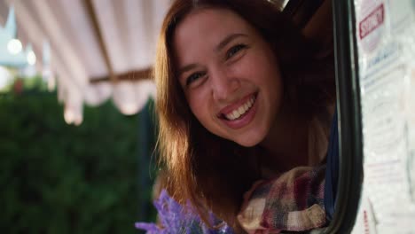 Close-up-portrait-of-a-happy-brunette-girl-sticking-her-head-out-and-looking-out-of-a-trailer-window-during-her-picnic-at-a-camp-outside-the-city-in-the-summer