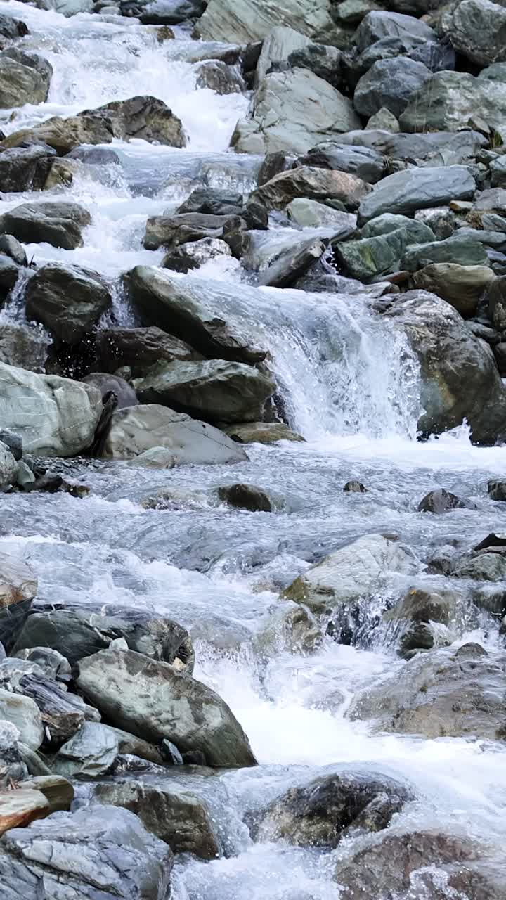 Un limpido ruscello di montagna scorre rapidamente su grandi rocce in un ambiente naturale e aspro. La luce del giorno illumina l'acqua e le pietre. La telecamera rimane stabile per tutta la durata.
