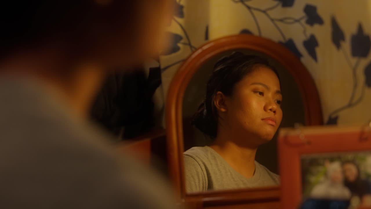 Immagine nello specchio di una ragazza asiatica indonesiana che sospira, triste, e ha spento la luce.