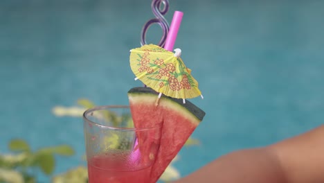 woman holds drink against pool with blue rippling water