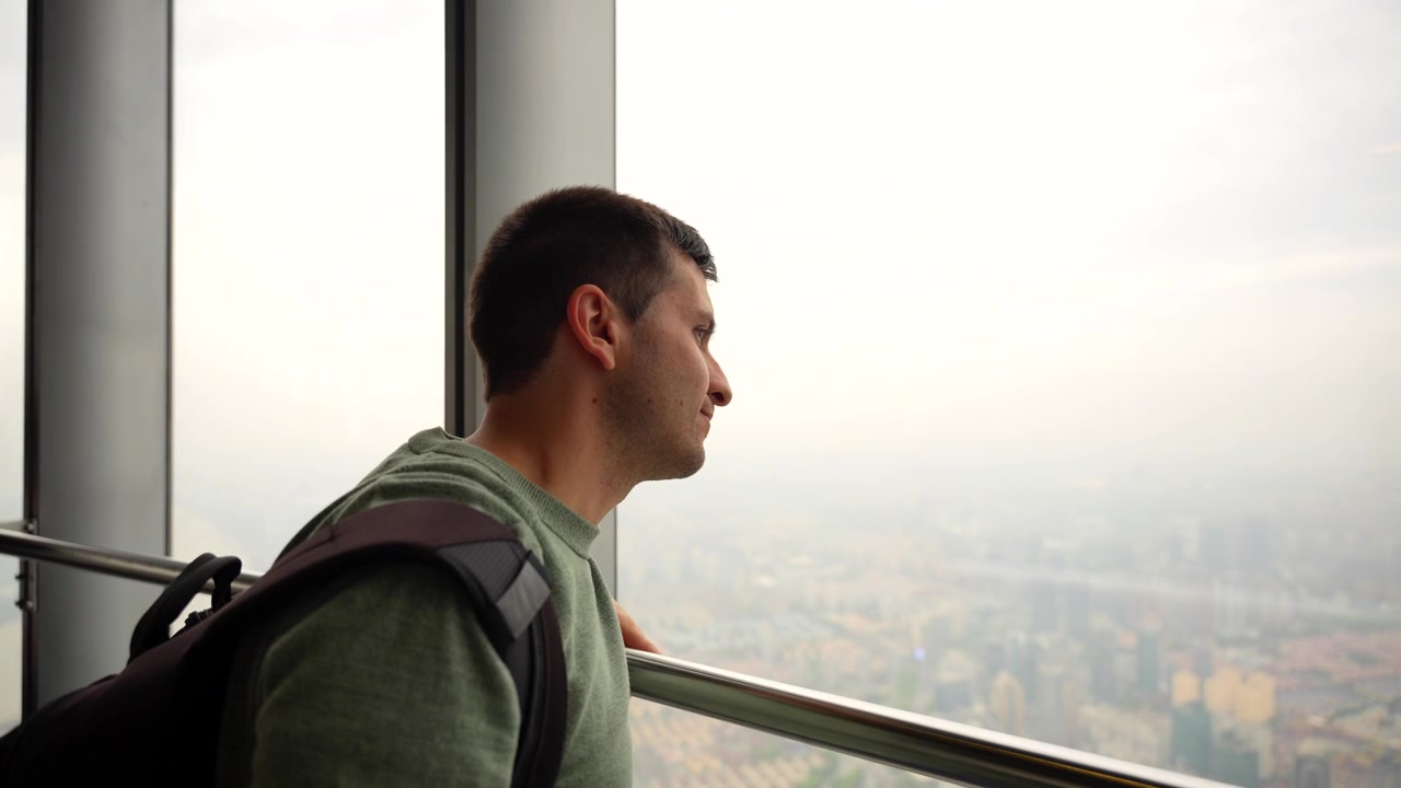Plano médio de homem caucasiano com mochila olhando para a cidade de Xangai do mirante de um arranha-céu. Pudong, China