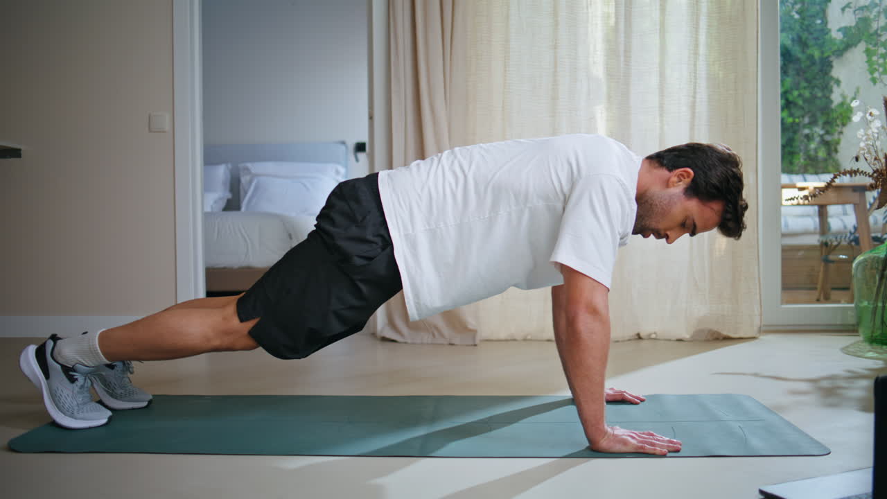 Guy making sport exercises at daily workout at modern apartment. Athletic man