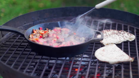 person making indian food and naan bread in a frying pan outside while campling