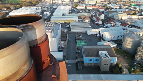 close drone footage of rusty power station chimney panning up to reveal industrial area and vale castle guernsey lit by late afternoon sun