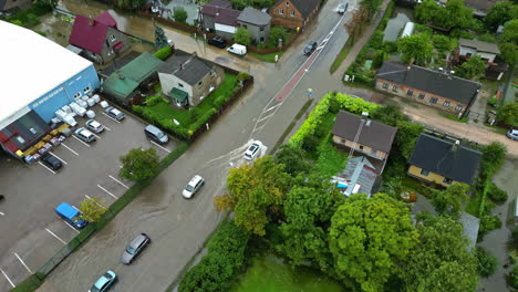 drone aerial view of car vehicles driving through flood water on wet road street hazard in town suburb rural residential community neighbourhood damage weather flood zone