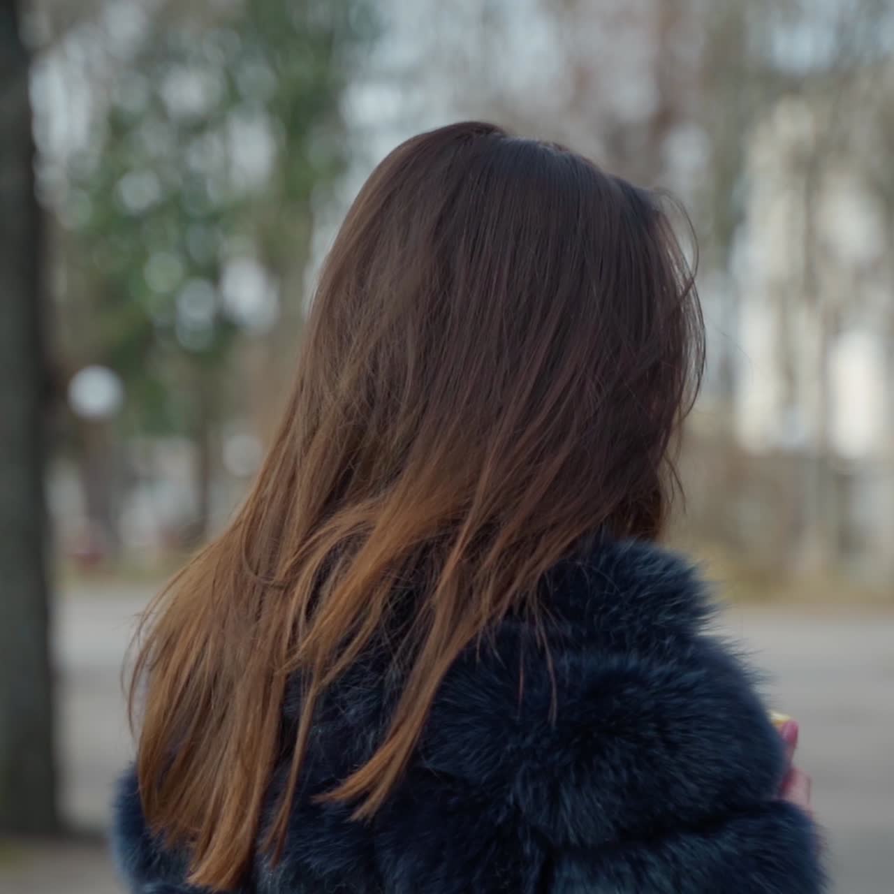 Attractive young woman with a plastic glass outdoors. Portrait of a charming girl with long dark hair in fur coat posing on camera in the park.