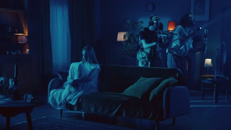 woman terrified as men in tactical gear enter her dimly lit home