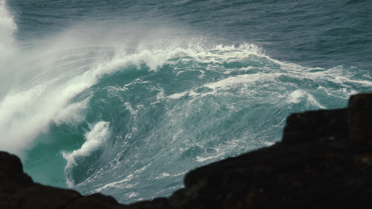 Looking through the rocks at a large, heavy wave breaking in slow motion