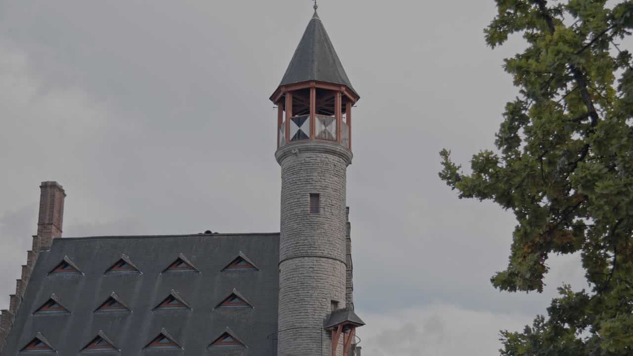 A close-up architectural shot of a historic building in Ghent, Belgium, dominated by a prominent circular stone turret with a crenellated upper section and a steeply-pitched conical roof