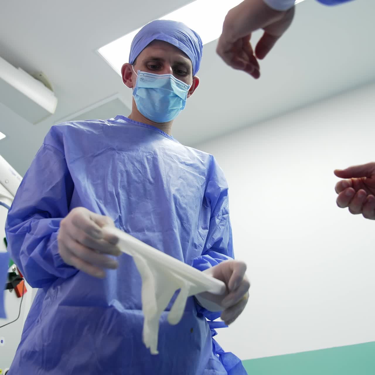 Male assistant helping the surgeon to put on latex gloves. Preparing for surgical operation. Low angle view