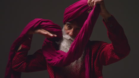 Fotografía-De-Estudio-Con-Iluminación-Tenue-De-Un-Hombre-Sikh-Mayor-Con-Barba-Atando-Una-Tela-Para-Un-Turbante-Contra-Un-Fondo-Oscuro-10