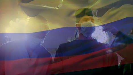 Animation-of-waving-colombia-flag-against-team-of-surgeons-performing-surgery-at-hospital