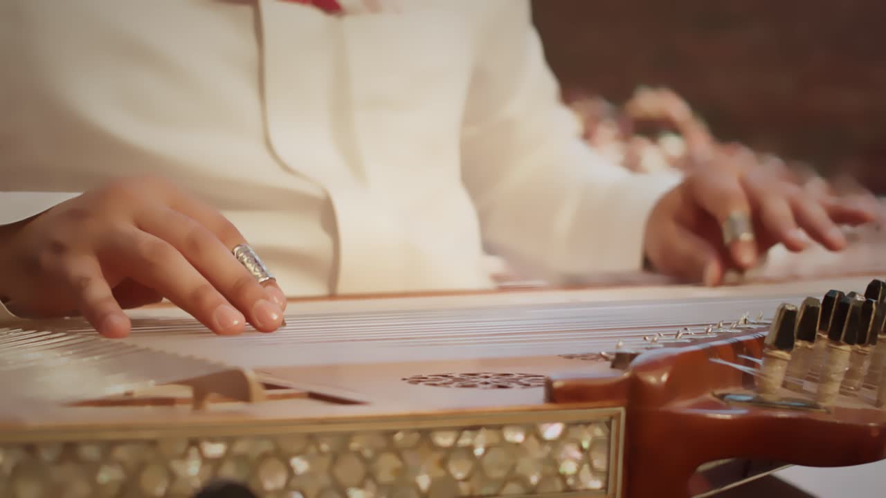 Primo piano di mani che suonano un qanun tradizionale mediorientale, uno strumento a corde comunemente usato nella musica saudita e araba