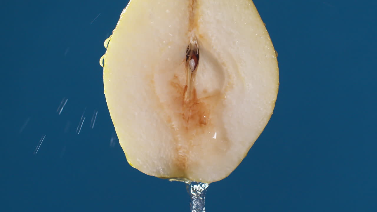 Yellow half pear on a blue dark background with drops of water rolling down the pear and flowing splashing with isolated background